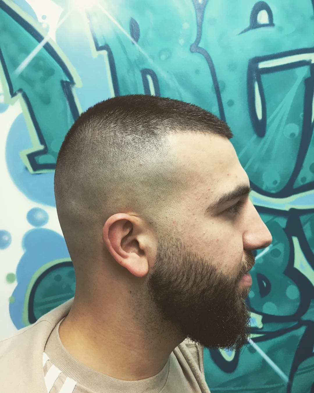 Buzz Cut mit High Fade und vollem Bart vor Graffiti-Wand
